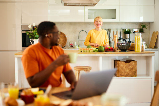 一个非裔美国人一边在家享用早餐一边使用笔记本电脑图片下载