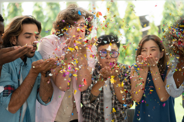 一群多民族的朋友在聚会上玩得很开心，吹彩纸图片下载