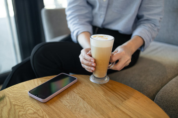 幸福美丽成功的商业女性的肖像拿着一杯咖啡杯心形拉花泡沫，而坐在桌子上用笔记本电脑远程工作的新网页设计项目。高质量照片图片下载