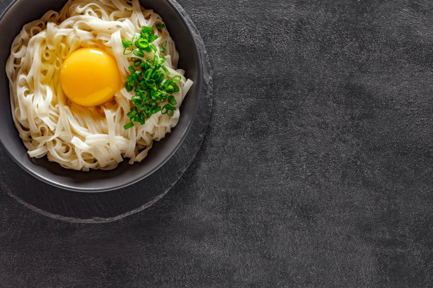 乌冬面用生鸡蛋和草药煮熟，板岩石盘圆形，深色背景，俯视图图片下载