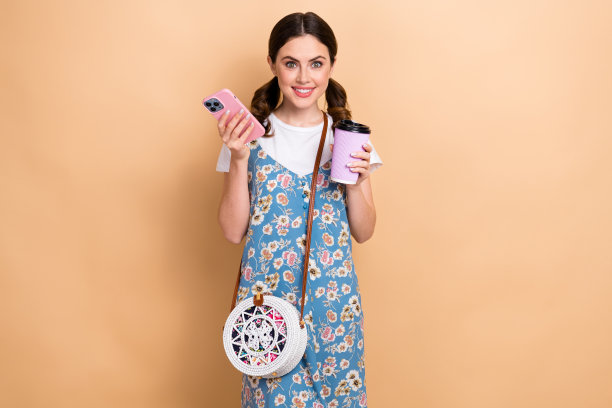 照片的年轻魅力有趣的女士穿着夏装萨拉芬钱包拿手机喝卡布奇诺博客孤立的米色背景图片下载