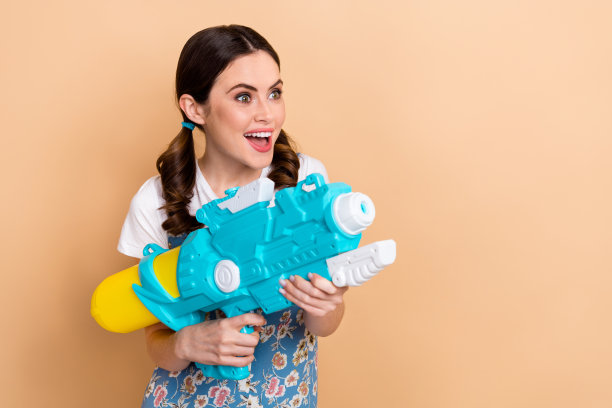 照片中的年轻有趣的玩耍无忧无虑的女孩拿着水枪飞溅射击她的朋友孩子空空间孤立的米色背景图片下载