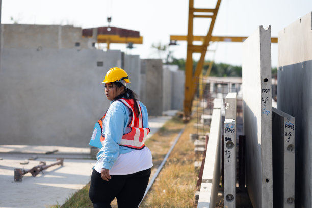 非裔美国妇女肖像。大码女工戴着安全安全帽头盔在重型预制混凝土墙制造工厂工作图片下载
