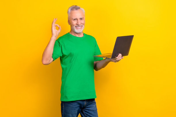 照片中英俊的老人牙齿微笑，拿着无线上网本，在黄色的背景上显示出好的标志图片下载