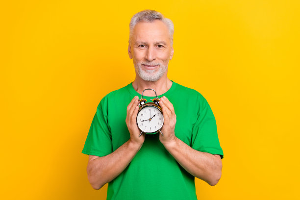 照片正面漂亮的老年男子手臂持有示范古钟响钟隔离在明亮的黄色背景图片下载