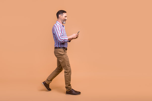 全尺寸的个人资料照片，英俊的积极男子走路使用智能手机空的空间，广告隔离在米色背景图片下载