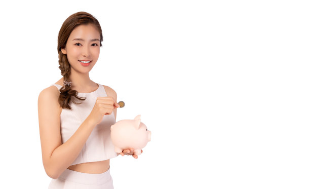 微笑的年轻亚洲女子把硬币放在存钱罐里，她梦想将来成为富人。穿着休闲服的年轻女孩拿着存钱罐，孤立在白色背景的复制空间里图片下载