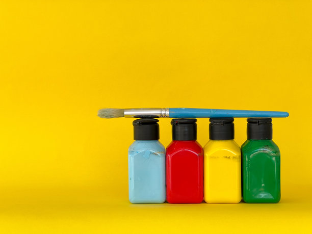 画笔和四个罐子，在黄色的背景上装着色彩鲜艳的丙烯酸颜料图片下载
