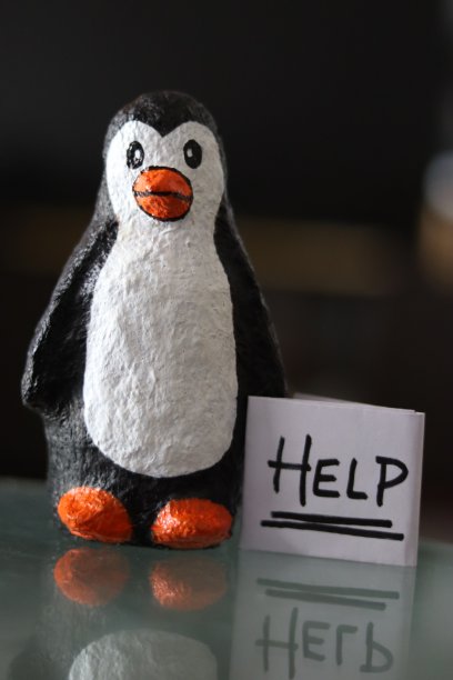 一只用纸浆做的小企鹅，手里拿着一张纸做的“帮助的标志”，旁边有散景图片下载