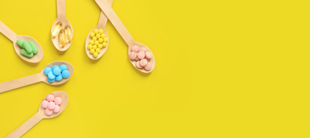 黄色背景上不同颜色的维他命装在木勺里，俯视图图片下载