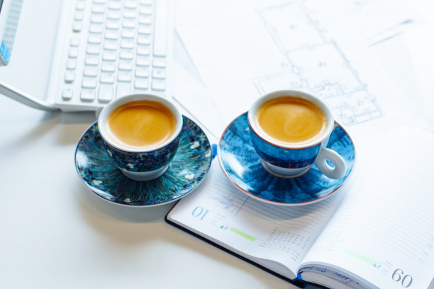 两个蓝色咖啡杯，日记本，纸质建筑图纸，蓝图，白色桌子上的键盘。室内设计师、建筑师的工作场所。俯视图图片下载