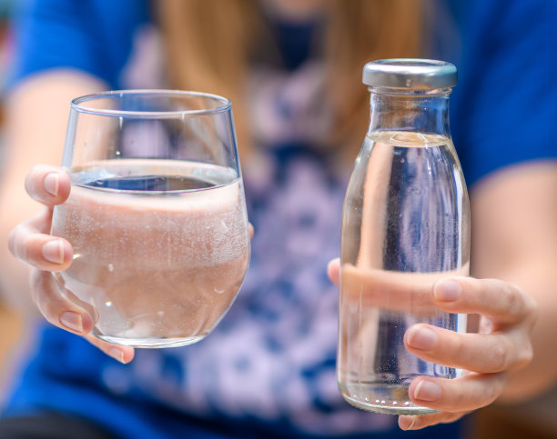 手里拿着一个玻璃杯和一瓶静止的矿泉水图片下载