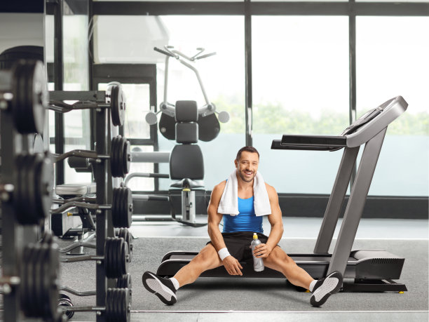 健美的年轻人坐在跑步机上，在健身房拿着一个瓶子图片下载