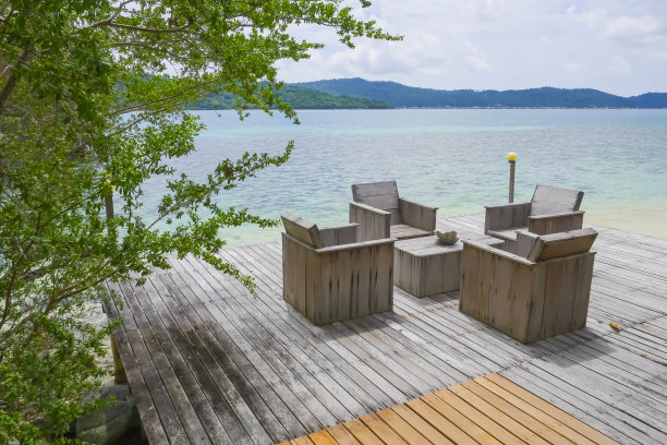 简单的户外酒店或度假村庭院用棕色的木制沙发家具和木桌，木地板，植物，蓝色的海滩海洋岛为背景图片下载