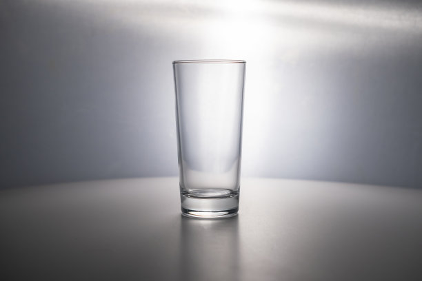 桌子上放着一个装水和果汁的空杯子，灰色的背景上有一盏漂亮的背光。一个地方的文字，复制空间。广告,横幅。气泡水健康营养图片下载