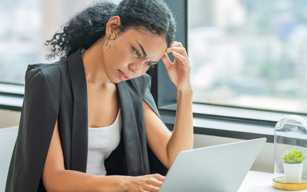 漂亮的非洲女商人坐在现代办公室的窗边，一边使用笔记本电脑，一边工作压力很大，不断收到投诉和问题。企业家的概念。图片下载