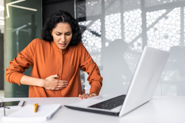 在办公室使用笔记本电脑工作的生病女商人，西班牙裔女性腹痛严重图片下载