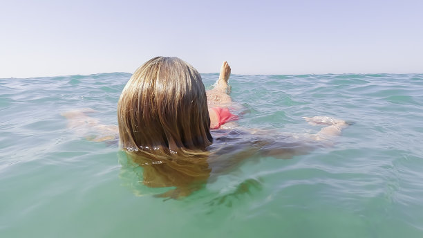 一个面目全非的成熟女人，夏天在海水里仰面游泳，用脚戏水。放松身心，幸福安康的理念。图片下载