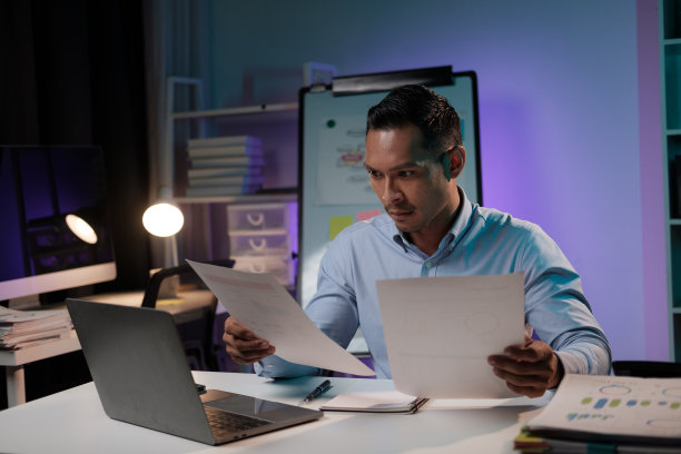 勤奋的亚洲商人专注于他的项目，手里拿着文件，晚上独自在办公室加班。图片下载