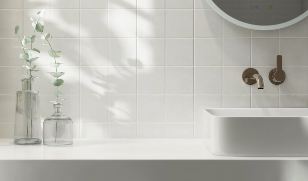 白色的梳妆台台面，带陶瓷面盆的方形墙砖，现代简约风格的水龙头，清晨阳光和阴影下浴室的细枝玻璃花瓶图片下载