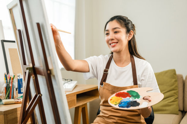 亚洲女艺术家正在用画笔和不同的丙烯酸颜料作画。作为艺术概念的女艺术家在创作工作室的画布上作画图片下载