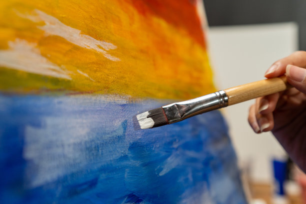 近距离的女性手艺术家在暗室温暖的光工作，用刷子和不同的丙烯酸颜料绘画。作为艺术概念的女艺术家在创作工作室的画布上作画图片下载