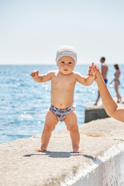 在海滩上，婴儿在妈妈的帮助下试图在石头码头上行走图片下载