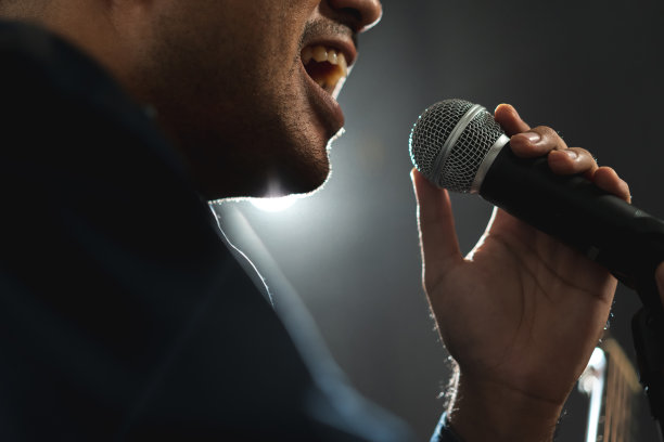 有魅力的歌手男子在舞台上唱着音乐，弹着吉他，聚光灯穿过音乐会的黑暗。音乐家在大厅里用灯光和烟雾现场表演。图片下载