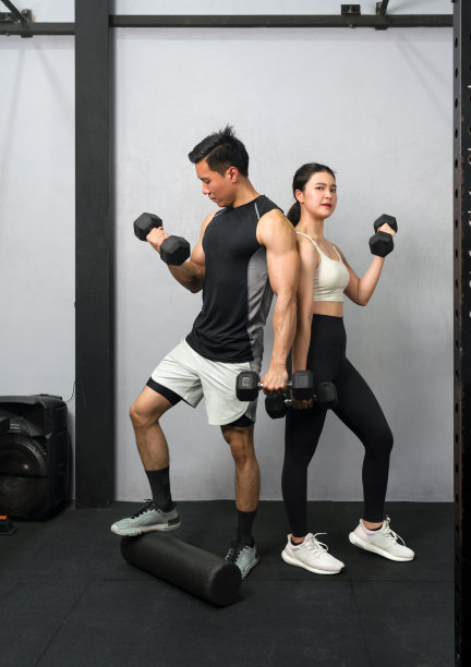 一对健康、专注的夫妇在现代健身房锻炼，每个人都坚定地握着一个钢哑铃。图片下载