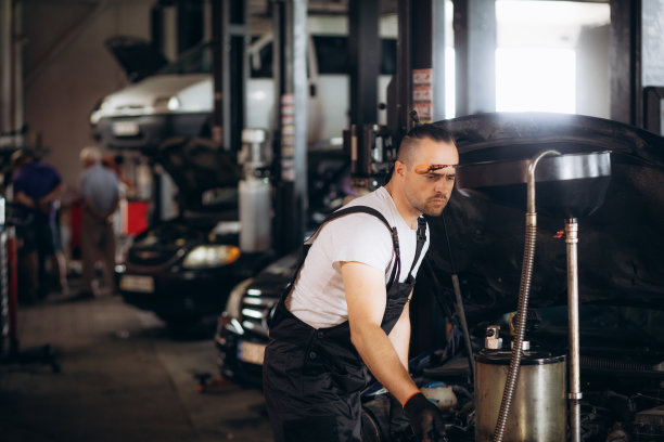 快乐的年轻机械师在一家汽车修理店换机油图片下载
