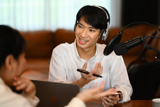 帅气的男电台主持人戴着耳机采访嘉宾，在家里的演播室录制播客图片下载