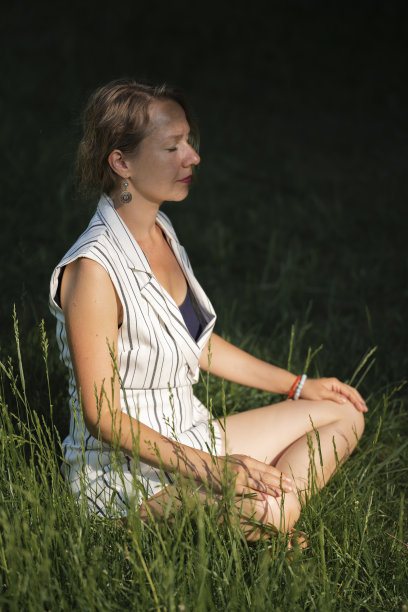 一个年轻的金发女子在午餐休息时坐在公园的草地上沉思。图片下载