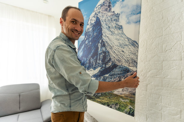 帆布印刷画廊包裹和干草室内装饰。女人把照片挂在白色的墙上。在法国比亚里茨市，手握着照片画布打印的岛屿图像图片下载
