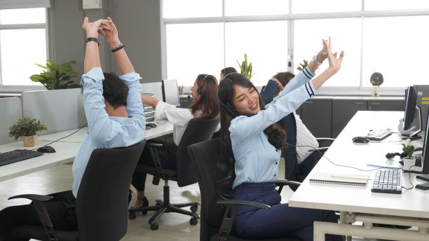 呼叫中心很累，年轻的成年员工一边工作一边戴着耳机伸展身体图片下载