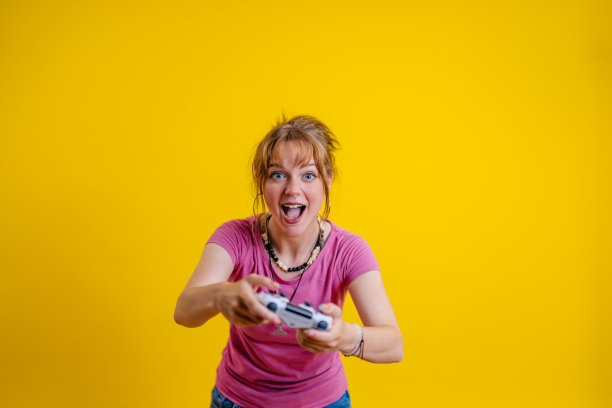 年轻女子在黄色背景下玩电子游戏图片下载