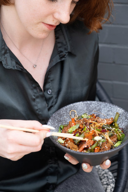 美丽的年轻女子品尝乌冬面配肉和炒蔬菜图片下载