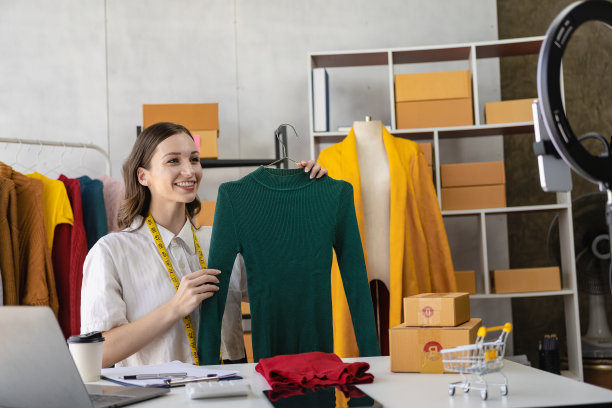 时尚博主概念年轻女性拿着衣服在流媒体视频、直播视频、社交媒体上展示和销售，她的唱片，通过数码相机在线销售。图片下载