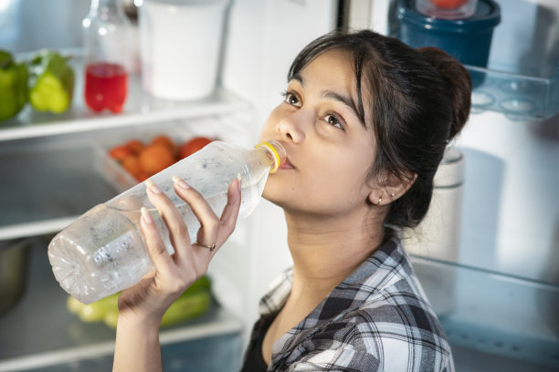 炎热的夏天，女子站在冰箱前喝凉水。图片下载