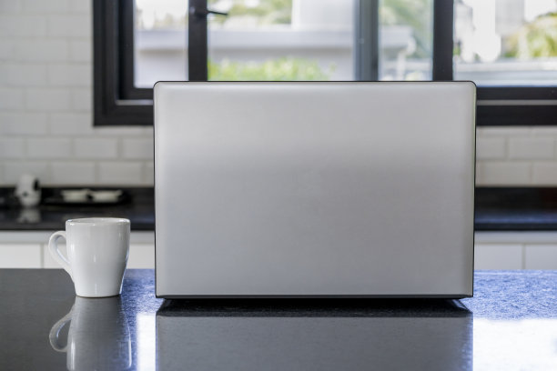 笔记本电脑和一杯咖啡在厨房岛。家庭办公室概念图片下载
