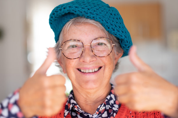 肖像微笑有吸引力的老年妇女戴着帽子和眼镜手势积极的迹象，双手看着相机图片下载