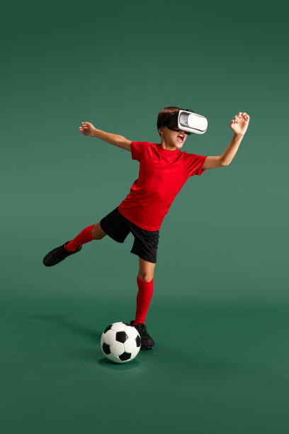网络游戏。小男孩，孩子戴着虚拟现实眼镜，在绿色的工作室背景下踢足球图片下载