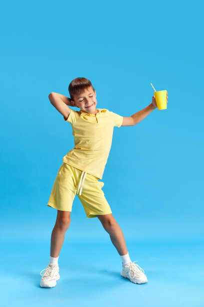 欢快的小男孩全身，孩子穿着休闲服摆姿势，在蓝色的工作室背景下跳舞图片下载