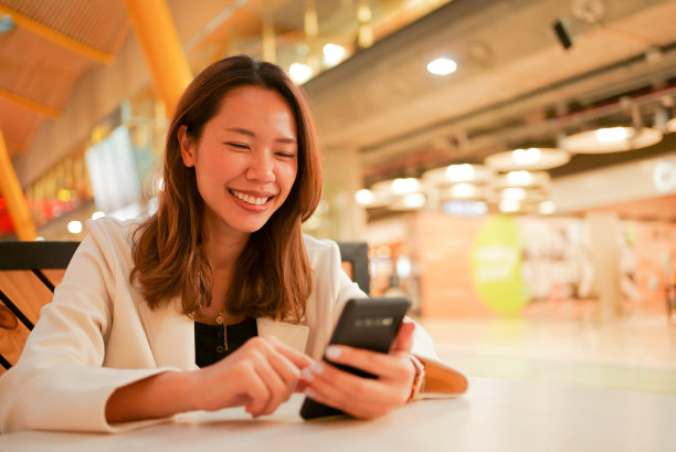 近距离商务女性微笑，同时使用智能手机与朋友或家人视频通话或查看社交媒体在机场等待时间的商务和放松的生活方式概念图片下载