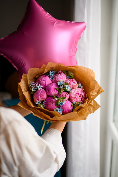 女子手里拿着粉红色气球背景上用手工纸包着的豪华花束图片下载