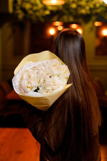 身穿深色大衣的黑发女子手持一束白色郁金香图片下载