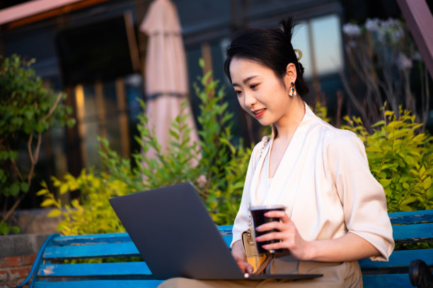 亚洲年轻女子坐在椅子上，使用笔记本电脑在城市公园图片下载