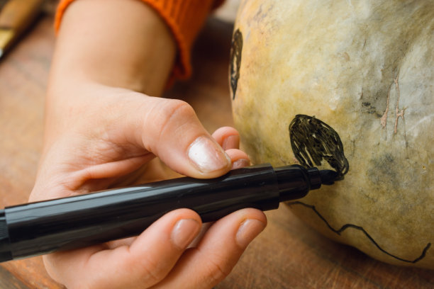 万圣节南瓜上用黑色马克笔画的难以辨认的白种人的手特写图片下载