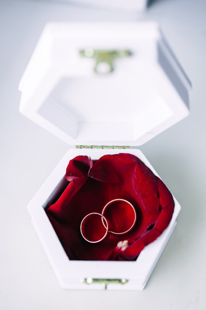 两个经典的金婚戒放在一个白色的盒子里，放在一朵红色的花上。婚礼细节图片下载