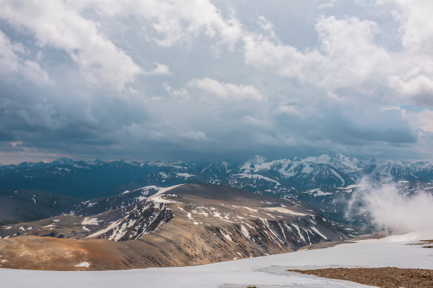 令人敬畏的顶景透过云层到高雪山。风景优美，低云中有美丽的雪山。大气的高山景观，从石山到雪山范围与低云。图片下载