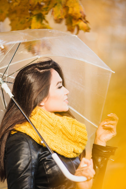 在明黄色模糊的背景下，伞下快乐微笑的女人图片下载